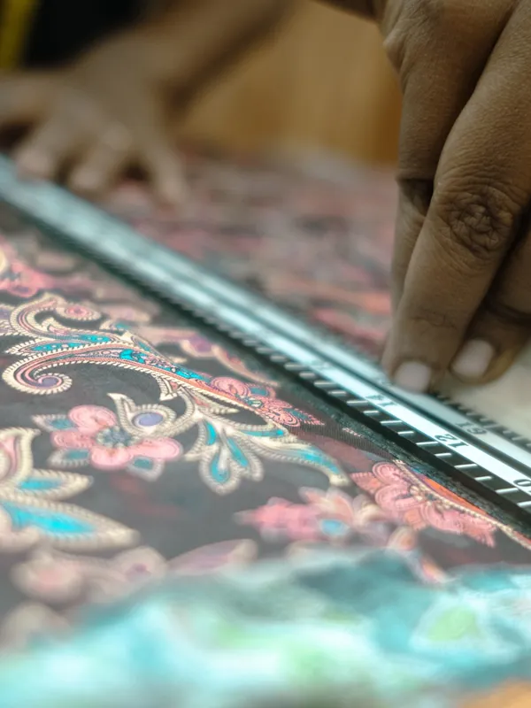 Hands cutting paisley print fabric along a steel ruler